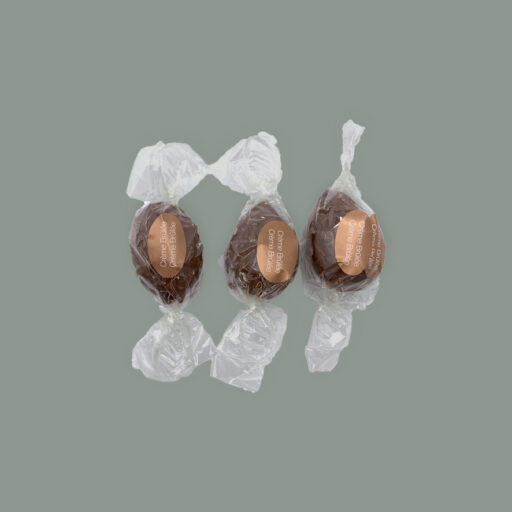 Drei Pralinen aus Vollmilchschokolade gefüllt mit Creme Brûlée Ganache. Einzel verpackt in durchsichtigem Stanniol mit Aufkleber