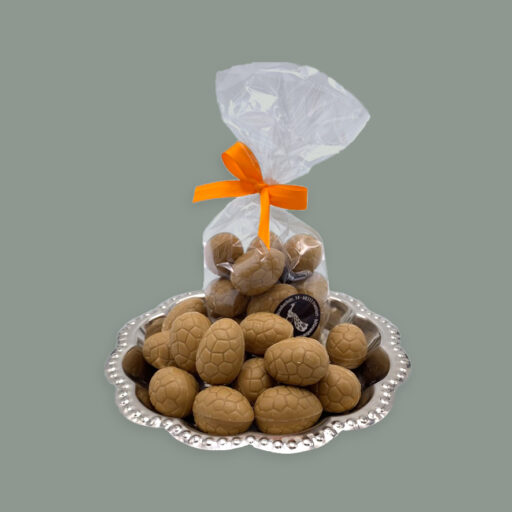 Valrhona Ostereier in Dulce Schokolade gefüllt mit Nougat. Dargestellt auf silbernem Tablett. Teils lose und in durchsichtigem Tütchen mit Schleife.