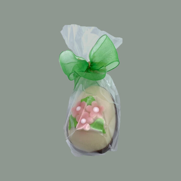 Osterei aus feinem Marzipan. Untere Seite hab getaucht in Zartbitterschokolade. Dekoriert mit Blumen aus Zuckerguss. Verpackt in durchsichtigem Tütchen mit grüner Schleife.