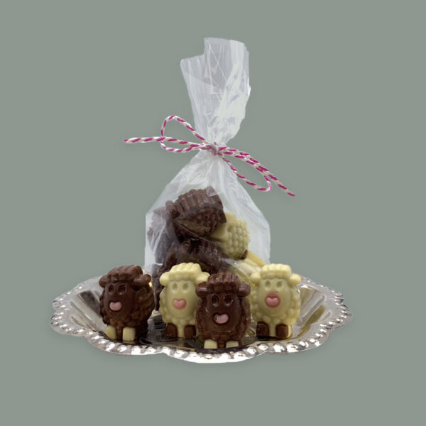 Kleine Schäfchen aus Vollmilchschokolade und Weißer Schokolade gefüllt mit Nougat. Dargestellt auf silbernem Tablett. Teils lose und in durchsichtigem Tütchen mit Schleife.