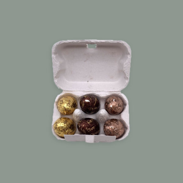 Kleine Pappschachtel im Stil einer Eierverpackung. Gefüllt mit 6 Ostereiern. Zwei aus weißer Schokolade, zwei aus Vollmilchschokolade und zwei aus Zartbitterschokolade