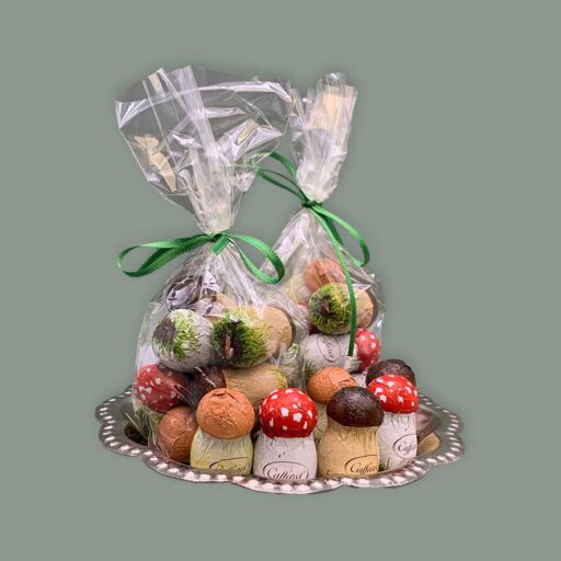 Caffarel Pilze aus Vollmilchschokolade gefüllt mit Nougat. Hier dargestellt auf silbernem Tablett, Zum Teil verpackt in durchsichtigem Tütchen mit grüner Schleife. Teils lose um die unterschiede zu erkennen. Einmal als Fliegenpilz, einmal als Champignon und einmal als Steinpilz